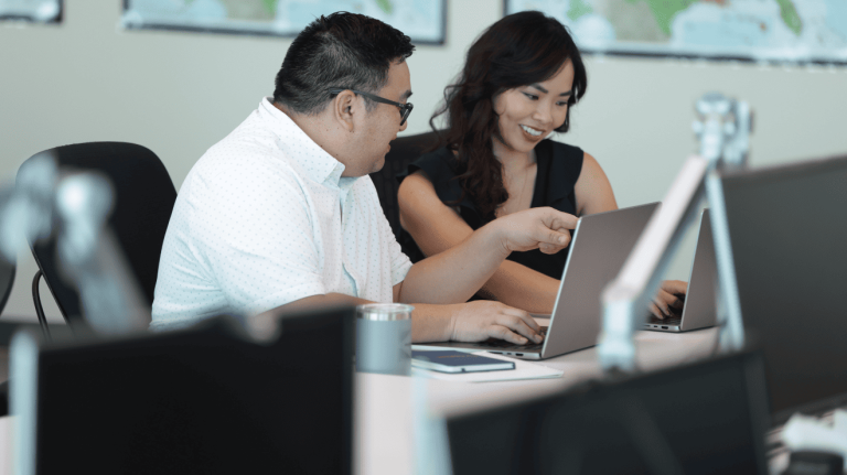 A man and a woman seated at a desk, engaged in work on their laptops, collaborating effectively.