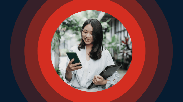A woman smiles while holding a tablet in one hand and looking at her phone with the other.