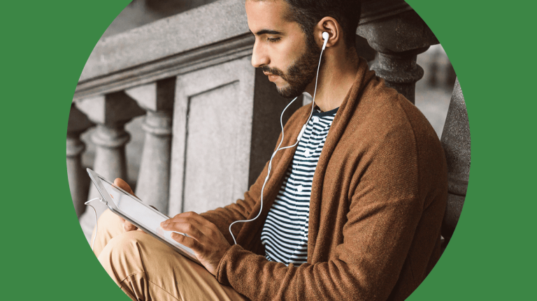 A man wearing headphones sits on a bench, focused on a tablet in his hands.