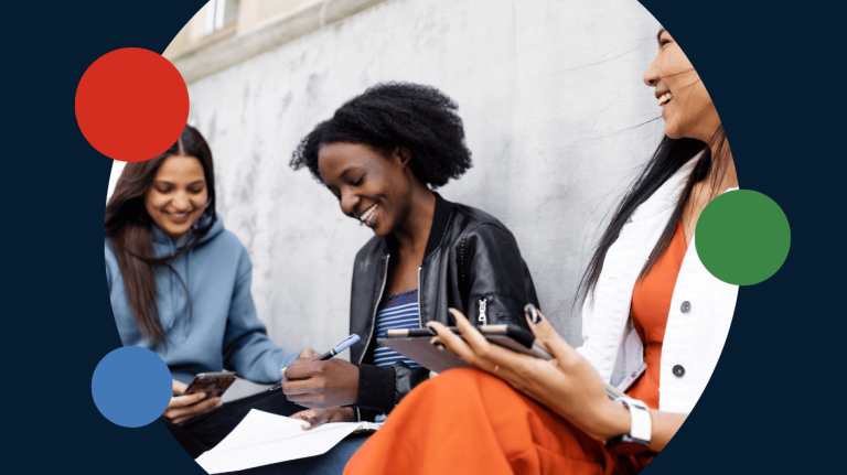 Three women sitting on a wall, each engaged with their smartphones, enjoying a casual moment together.