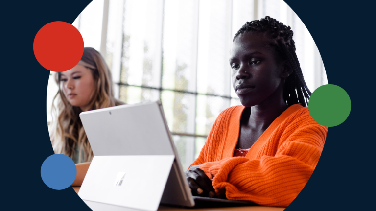 Two women seated at a table, collaborating on a laptop, engaged in discussion and sharing ideas.