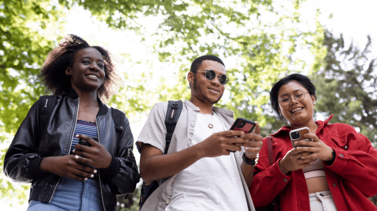 Three young people stand together, each holding a cell phone and engaging in conversation.