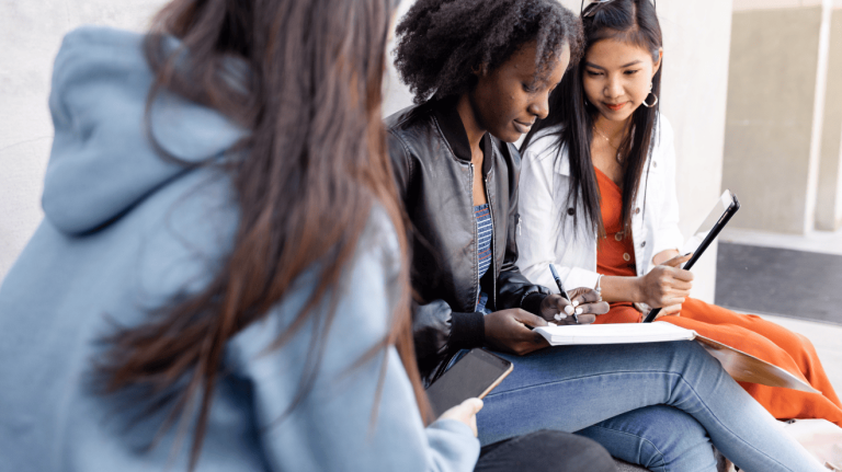 Three young women sitting on the steps of a building, engaged in conversation and enjoying each other's company.