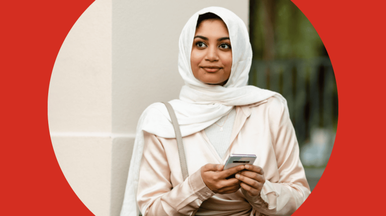 A woman wearing a hijab is holding a smartphone, appearing attentive and connected to her device.