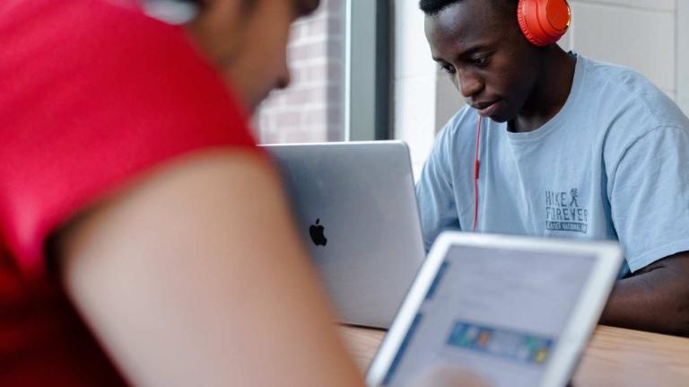 students sit at table, working on laptops