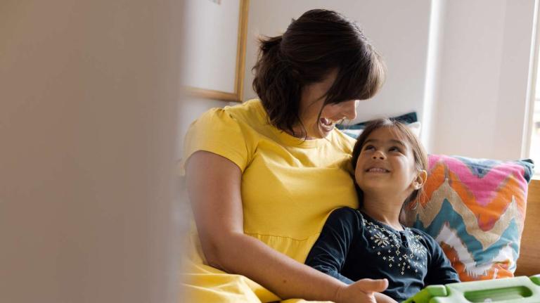 a mom sits with her daughter with a tablet