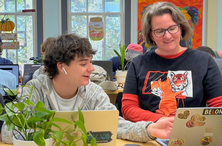 Kim Burlinson sits with a student at a table in her classroom