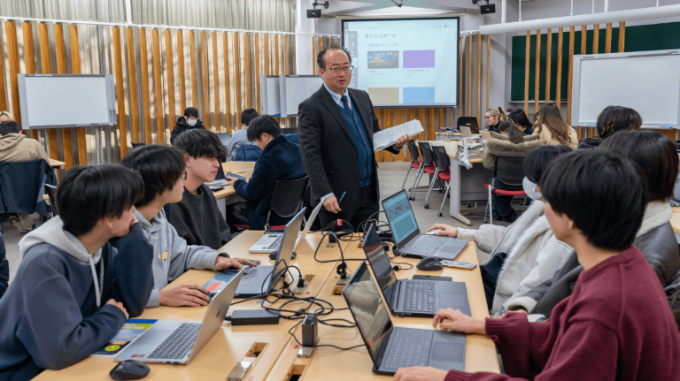 Educator leading an interactive university class, with students collaborating on laptops while using Canvas displayed on a shared screen at the front of the room.
