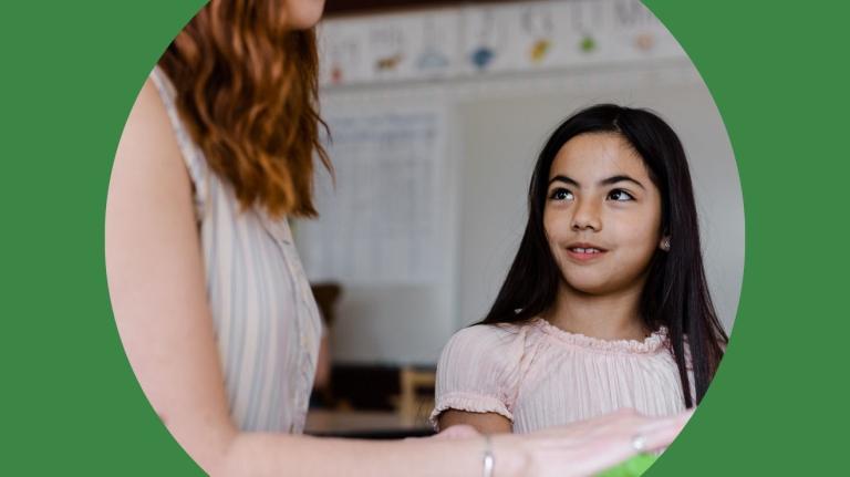 teacher sitting with a child at a computer in the classroom