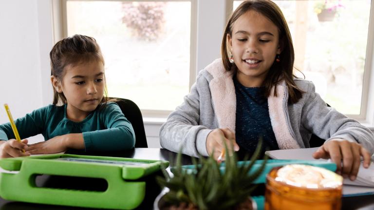 two sisters work on tablets at their dining room table
