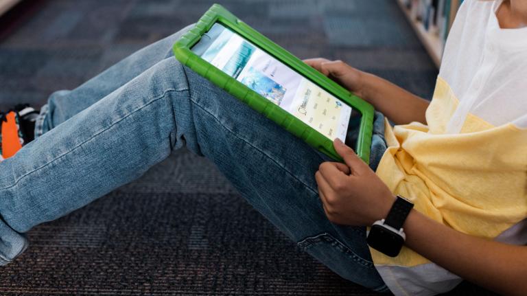 a student uses a tablet on the floor of a school library