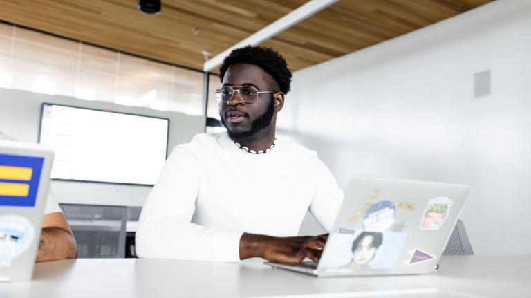 male student sitting at a table in front of an open laptop
