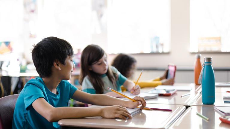 students in an elementary class write at a table