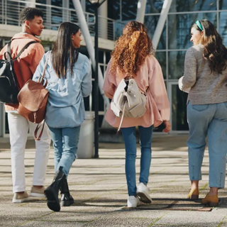 Four young people walking together in front of a modern building, engaged in conversation and smiling.