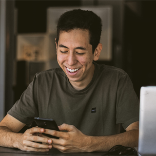 A man smiling while using a cell phone, appearing engaged and happy in a casual setting.