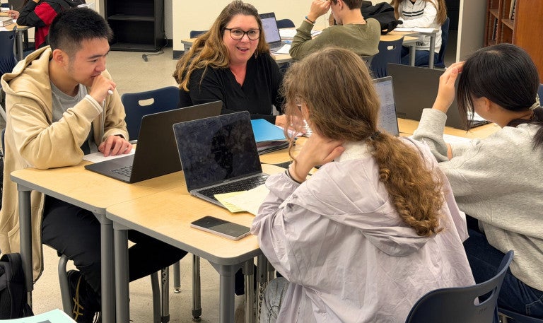 Meg Battey sits with three students at a table in her classroom