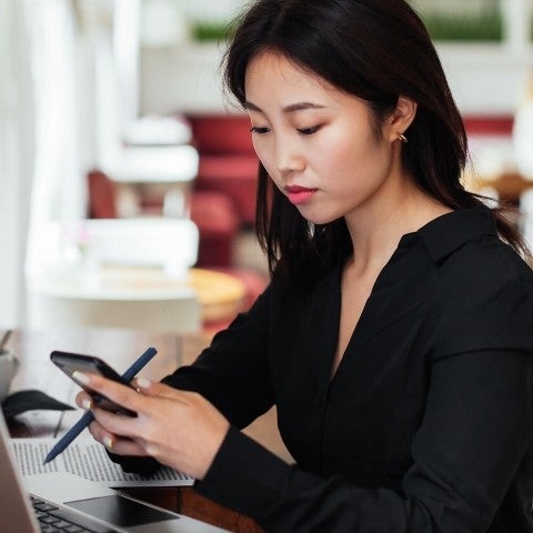 Person sitting at desk working on laptop looking at phone