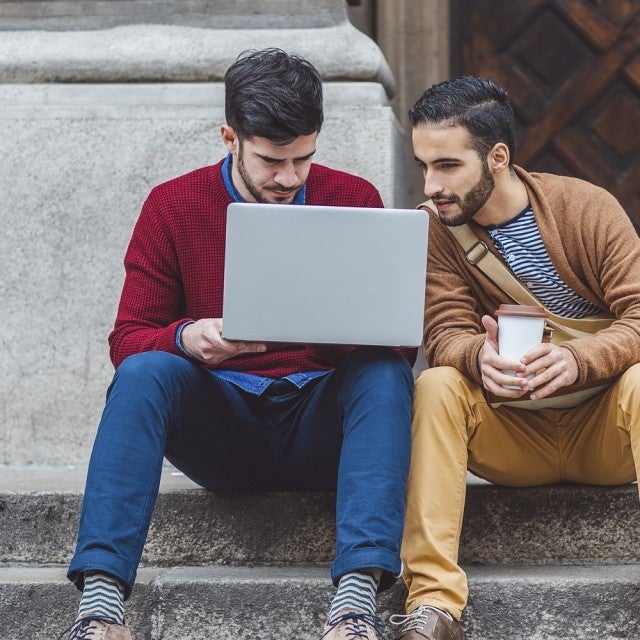 two people sitting on stone steps looking at a laptop