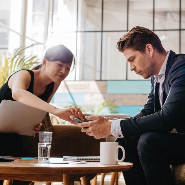 Two people sitting at coffee table working on phone
