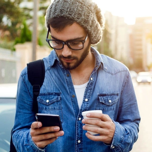 Person walking holding coffee and looking at phone