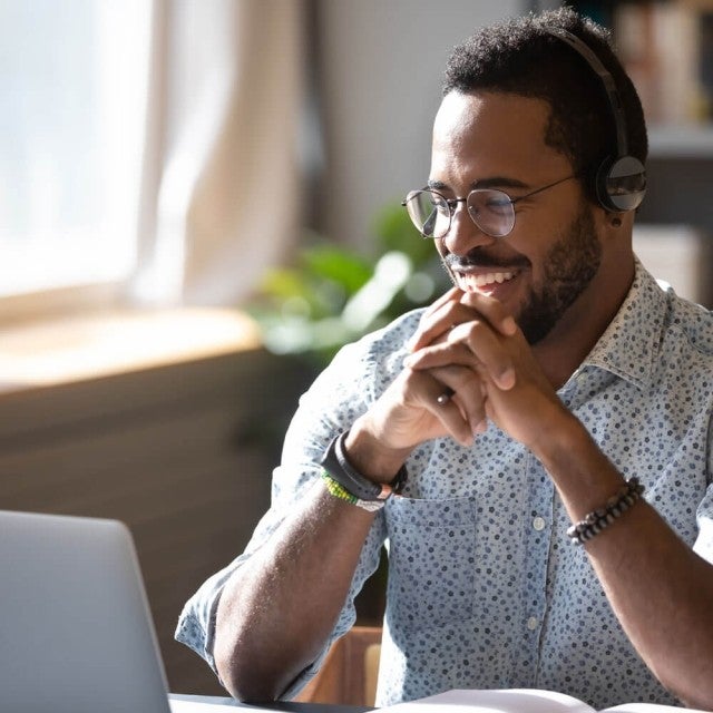 Person smiling and looking at computer with headphones on