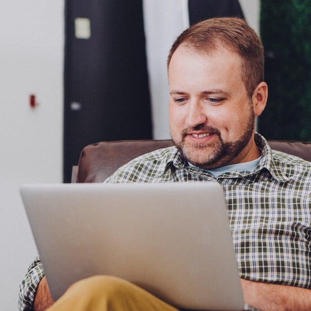Person smiling while sitting on armchair working on laptop