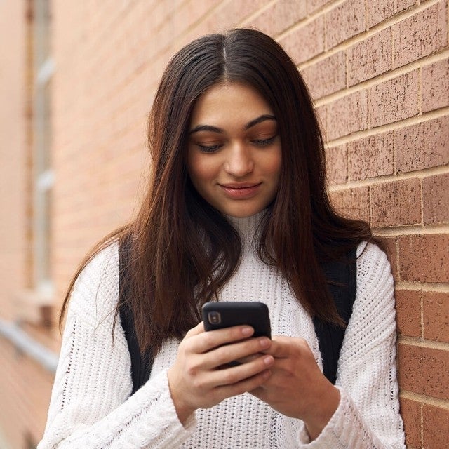 Student leaning against brick wall looking at phone