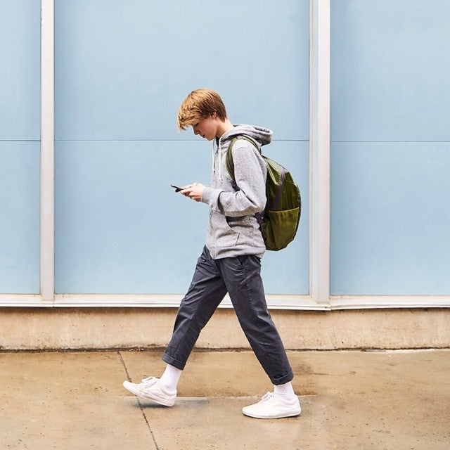 Student walking down street wearing backpack and looking at phone