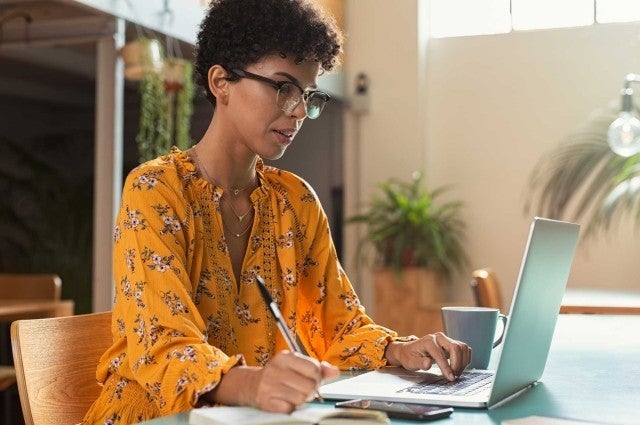 Woman in yellow shirt holding pen while using laptop