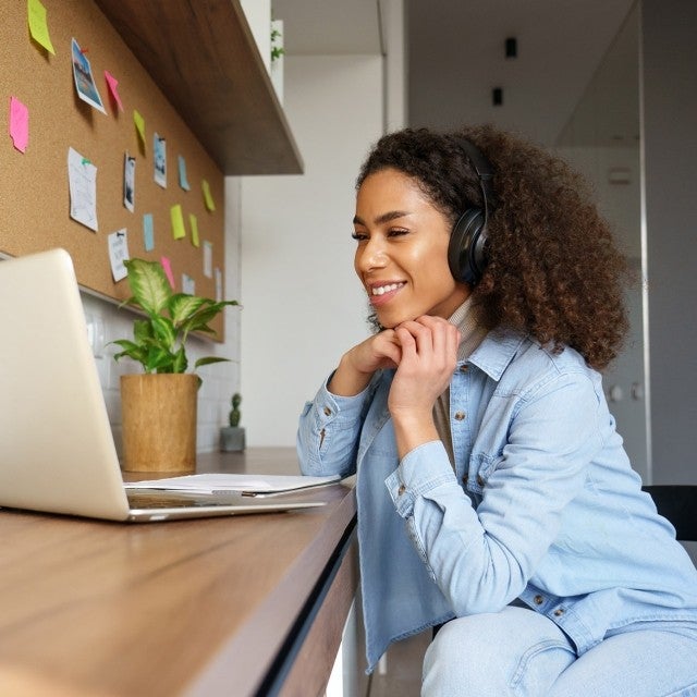 Woman smiling while wearing headphones listening to a computer at a desk