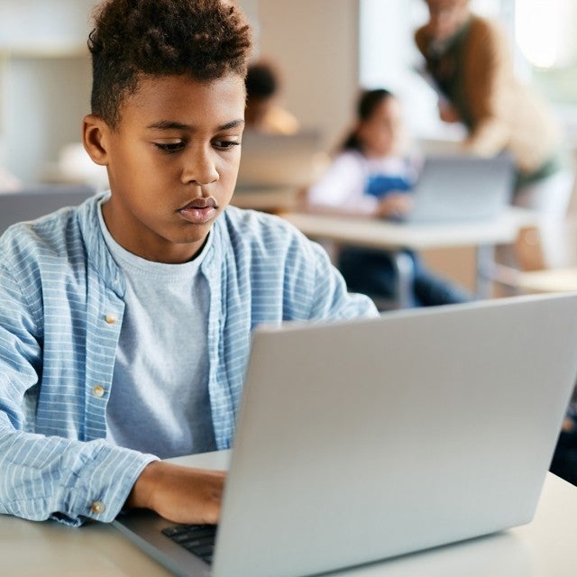 Child wearing blue long sleeve sitting at computer in classroom