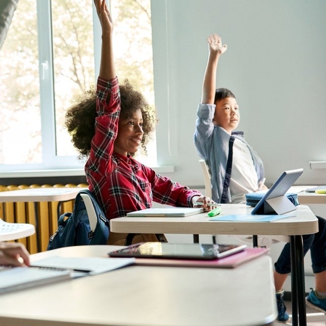 Children sitting at desks with raised hands