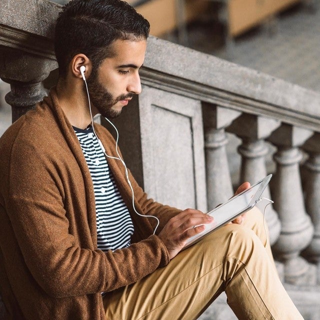 Man sitting on steps listening to ipad with headphones