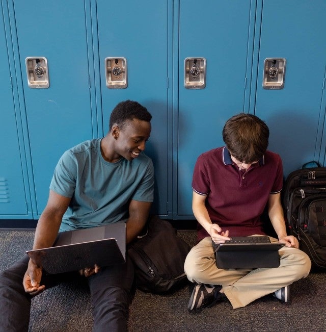 Kids sitting by lockers using Canvas LMS