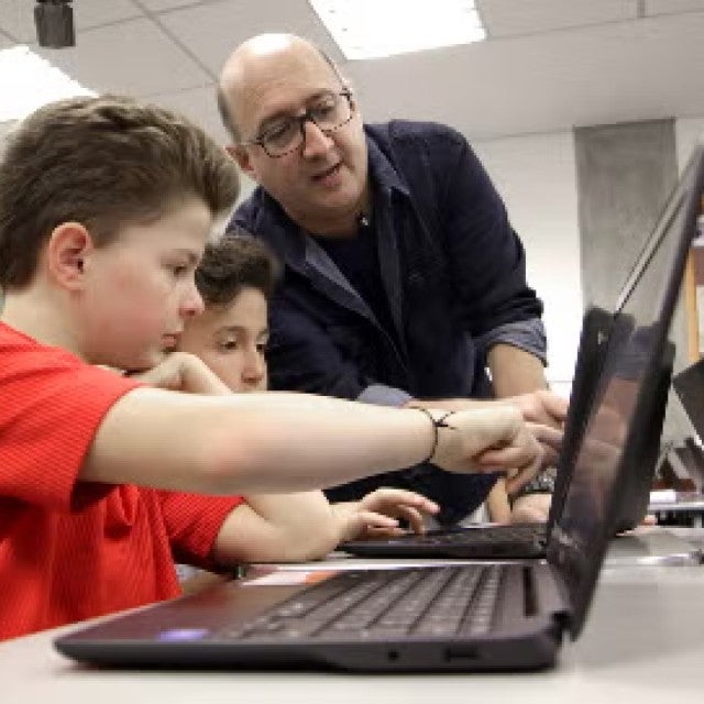 A teacher helping students through their course curriculum on laptops