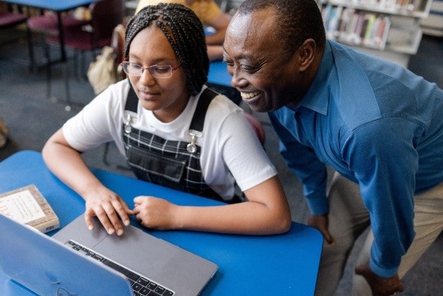 A teacher helping a student who is learning on a laptop.
