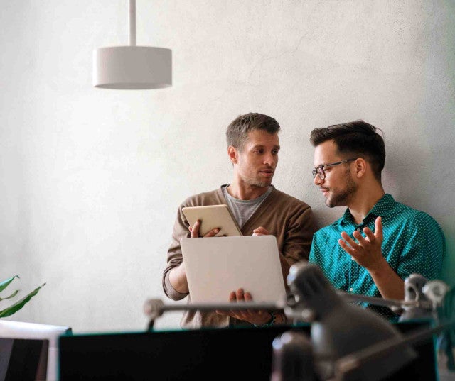 Two professionals chatting in front of a laptop in a sunny office