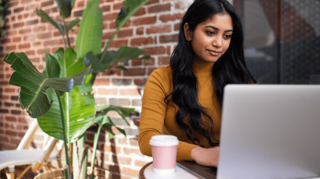 Adult learner using a laptop in a café setting, working independently with a coffee nearby.